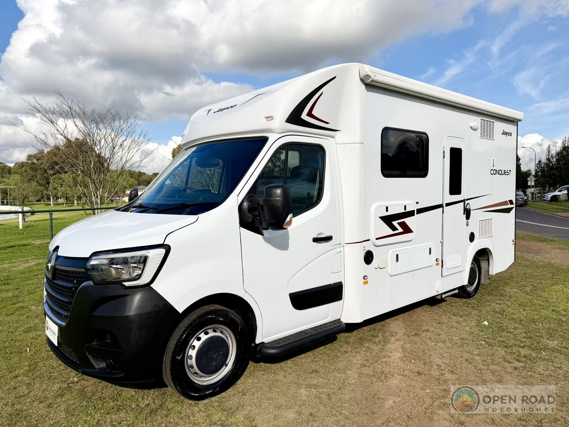 Front passenger-side 45-degree hero exterior of a 2025 Jayco Conquest RM20-5 motorhome, showing the Renault Master cab, Jayco branding, Conquest decal, white body with graphics, parked on grass